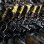 Revólveres com etiquetas amarelas dispostos em um suporte.