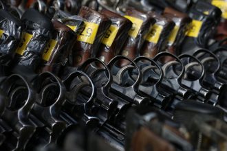 Revólveres com etiquetas amarelas dispostos em um suporte.