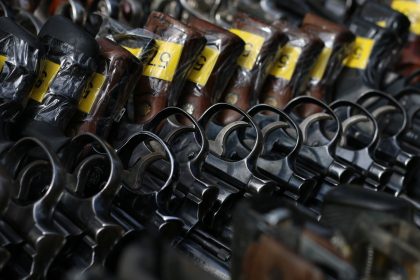 Revólveres com etiquetas amarelas dispostos em um suporte.