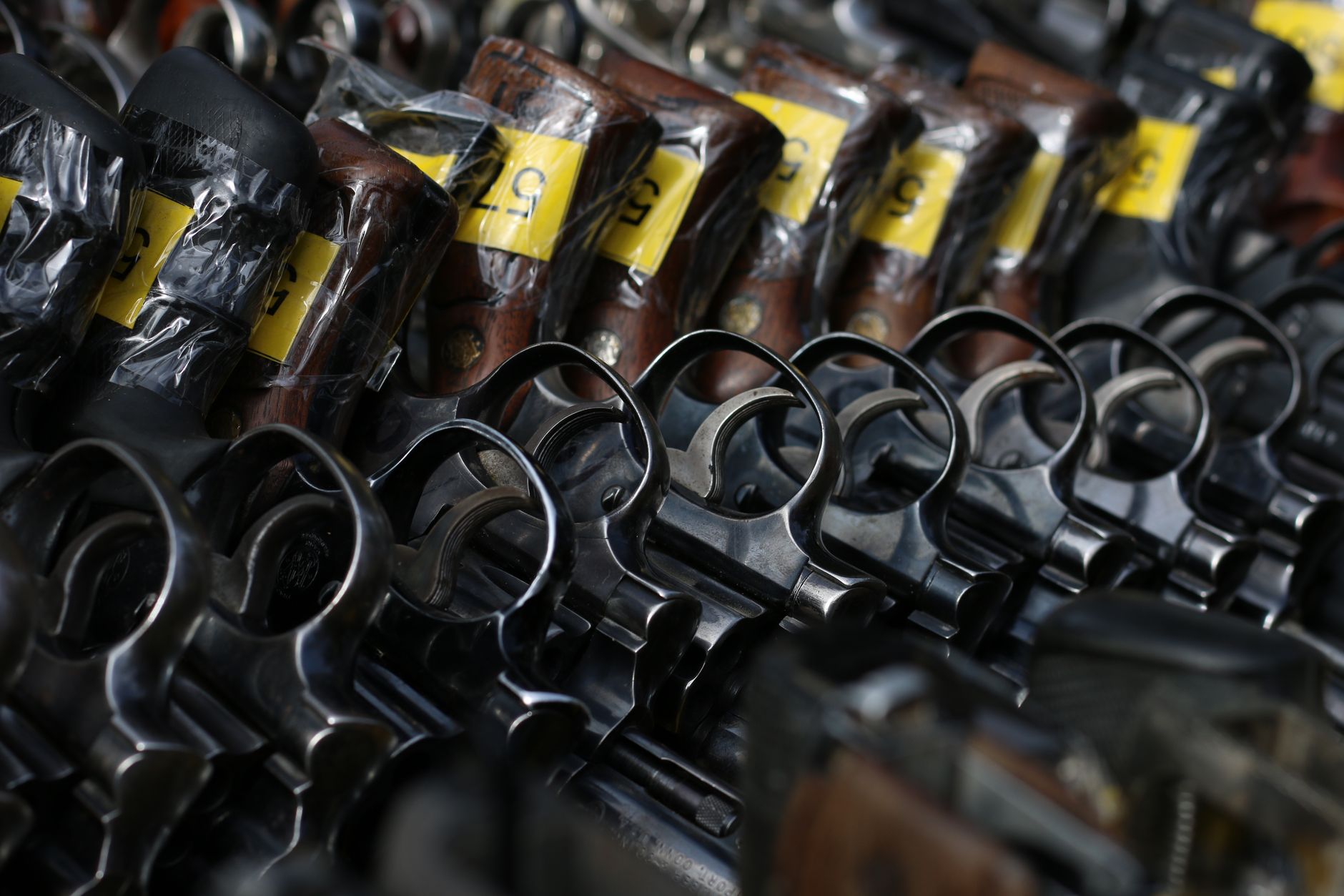 Revólveres com etiquetas amarelas dispostos em um suporte.