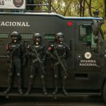 Agentes de segurança em equipamento tático ao lado de um veículo blindado durante uma operação.