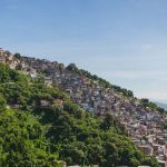 Vista aérea de uma comunidade em uma encosta arborizada do Rio de Janeiro, com casas densamente construídas.