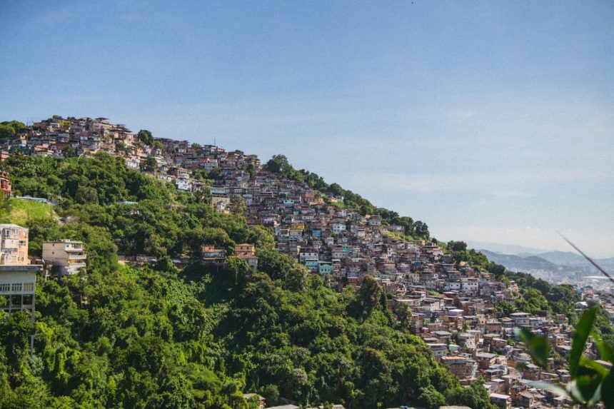 Vista aérea de uma comunidade em uma encosta arborizada do Rio de Janeiro, com casas densamente construídas.