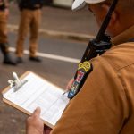 Policial fardado preenche uma prancheta durante atividade ao ar livre.