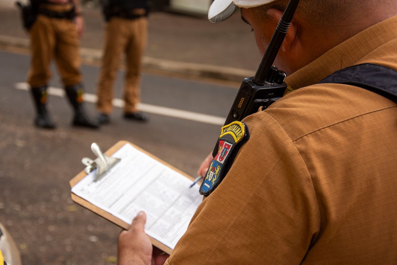 Policial fardado preenche uma prancheta durante atividade ao ar livre.