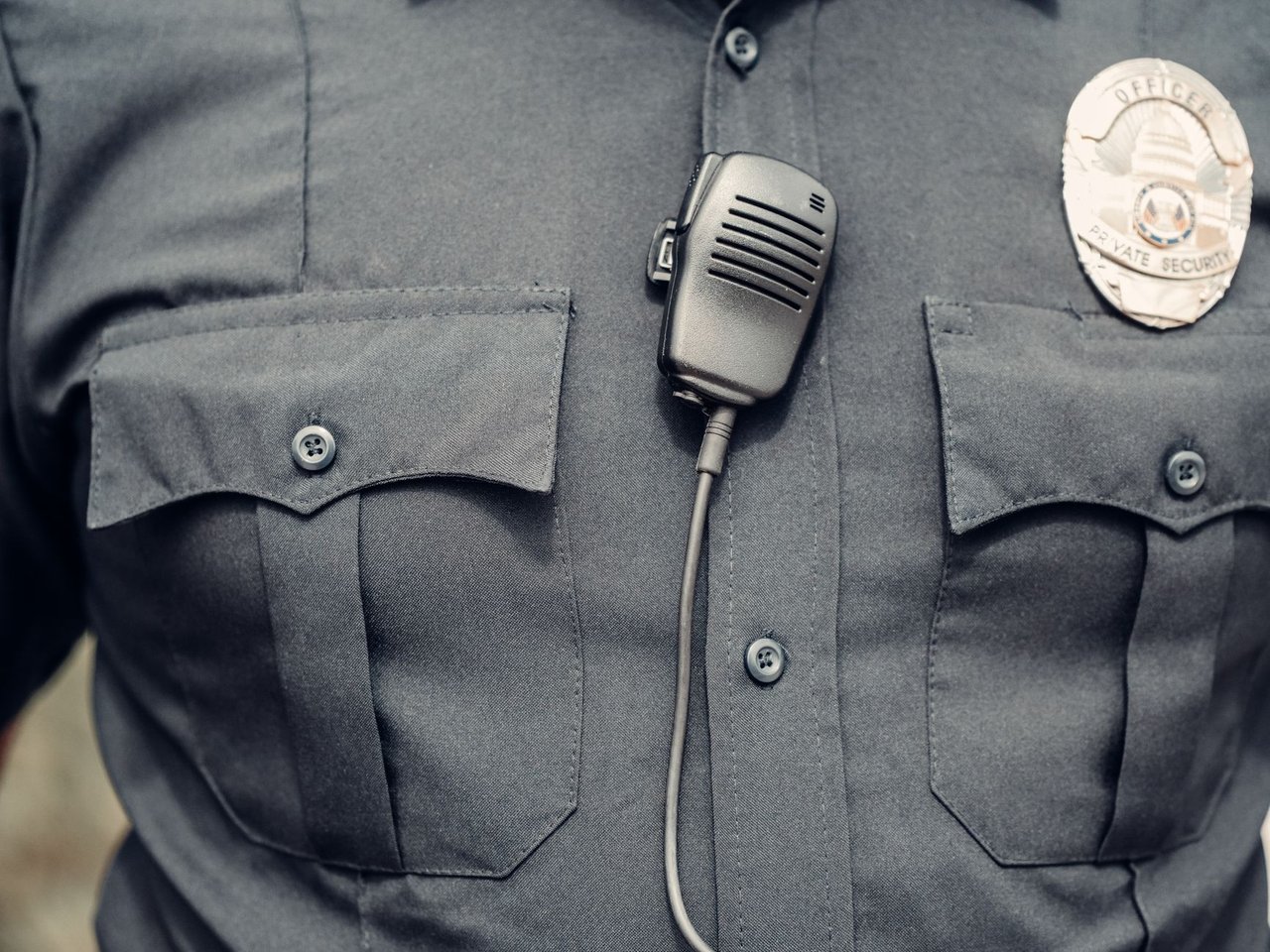 Close de uniforme policial com câmera corporal e distintivo.